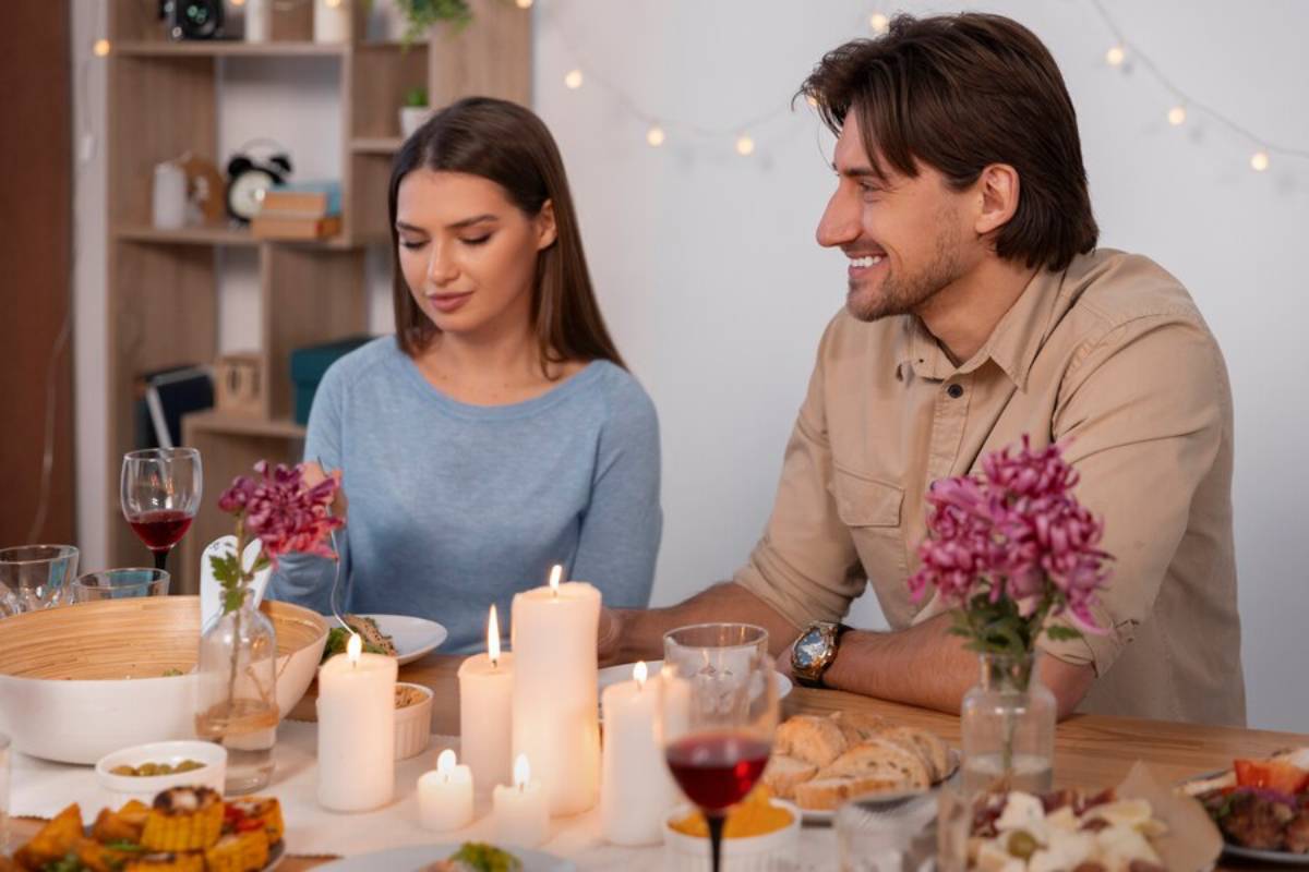 A couple enjoying a romantic dinner with candles and string lights in the background.